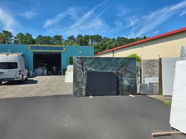 Rock Heads Granite Garden yard with stone slabs out front and the teal fabrication shop